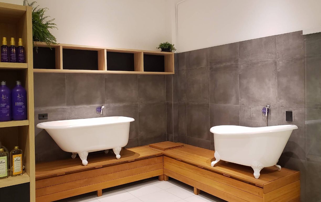 Sala de banho com duas banheiras estilo spa sobre bancada de madeira e produtos profissionais.